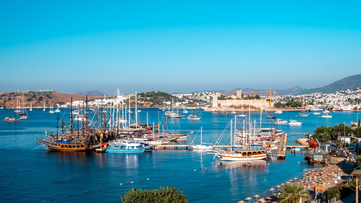 Panoramic view of Bodrum Marina and Bodrum Castle in Bodrum, Türkiye, featuring luxury yachts, traditional wooden boats, turquoise Aegean waters, and the historic waterfront skyline.