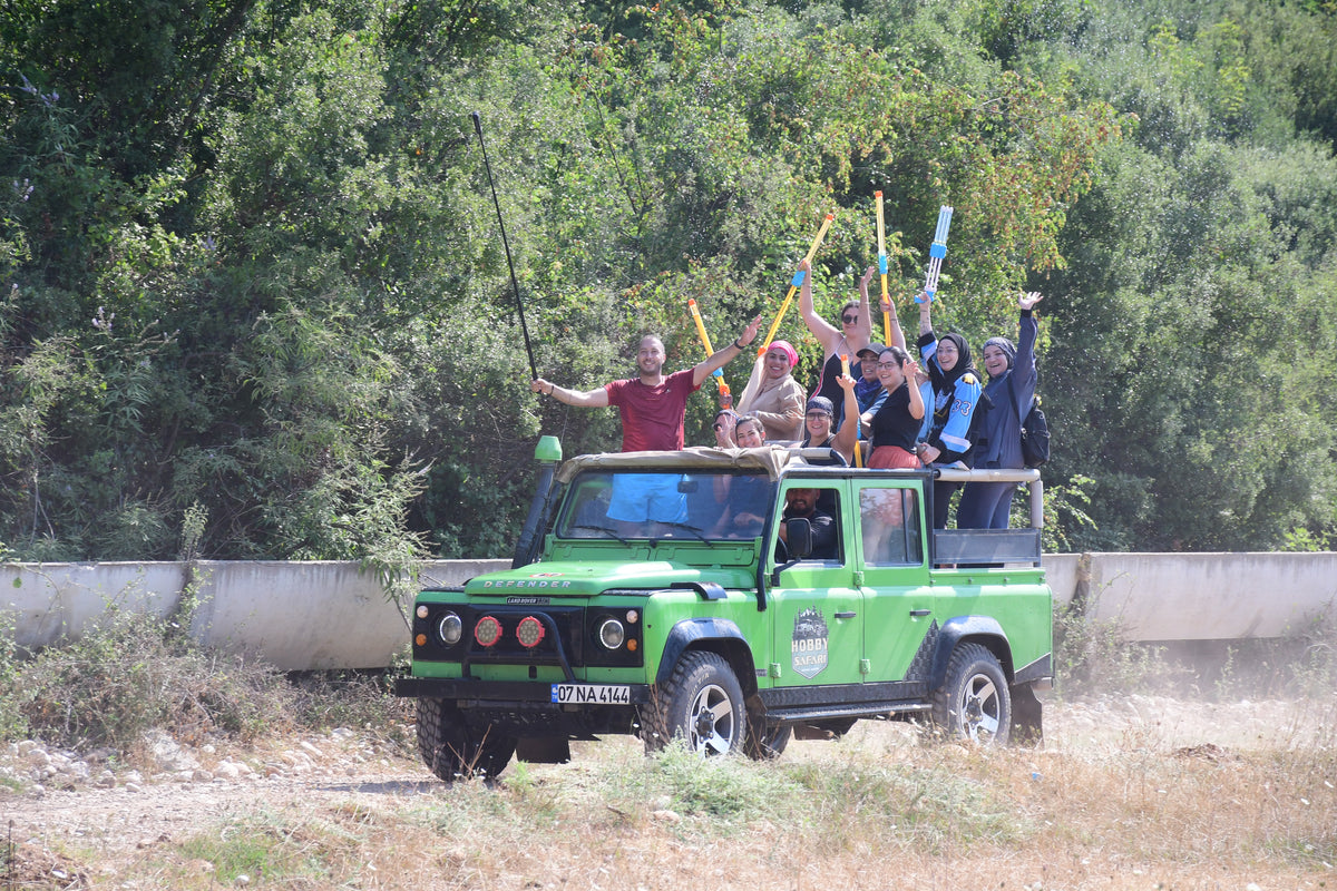 Green off-road vehicle in Antalya, Turkey with people waving flags on a road surrounded by trees