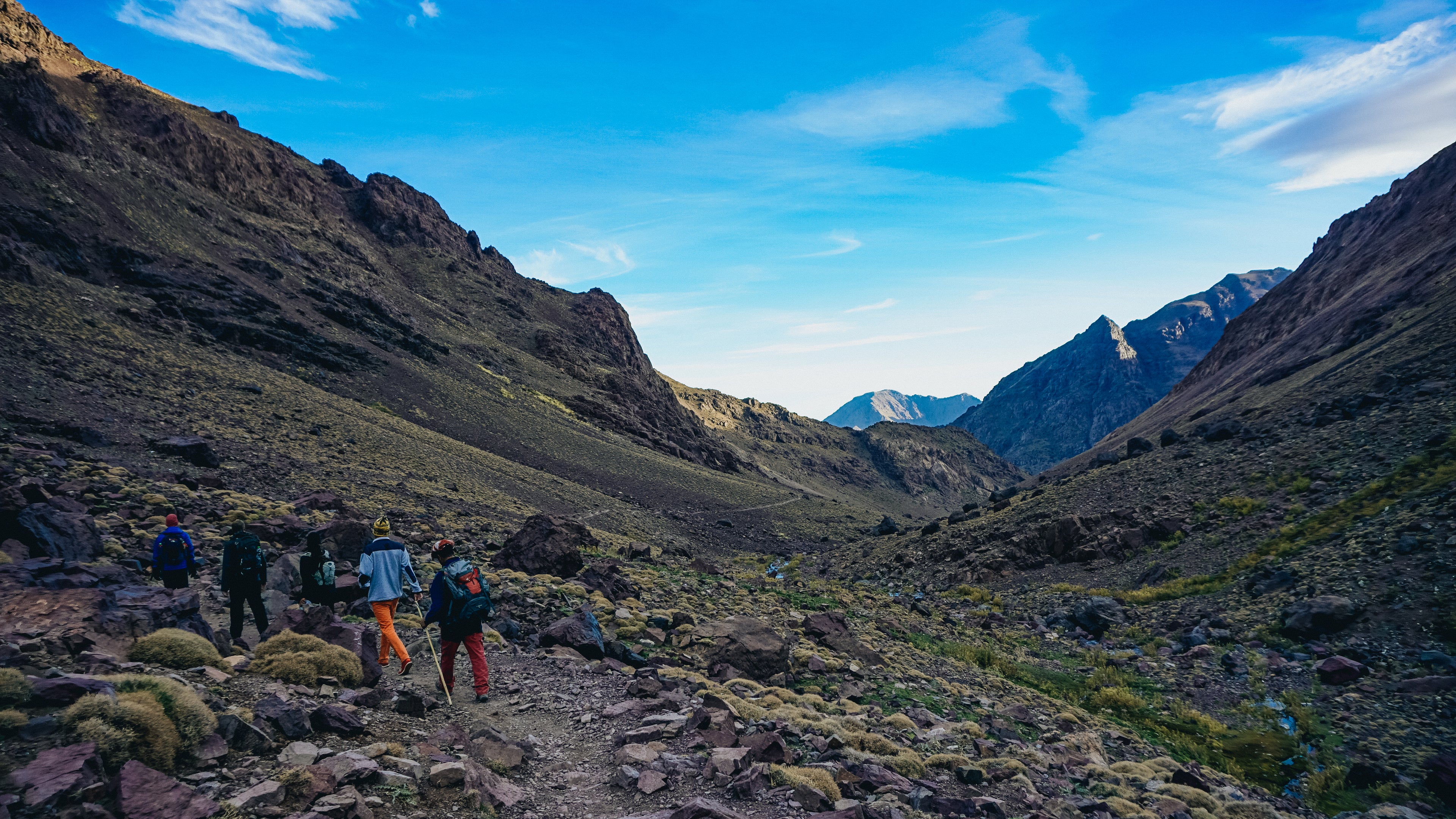 Group of hikers trekking through the rugged Atlas Mountains in Morocco, surrounded by rocky mountain landscapes, scenic valleys, and clear blue skies during an outdoor adventure.