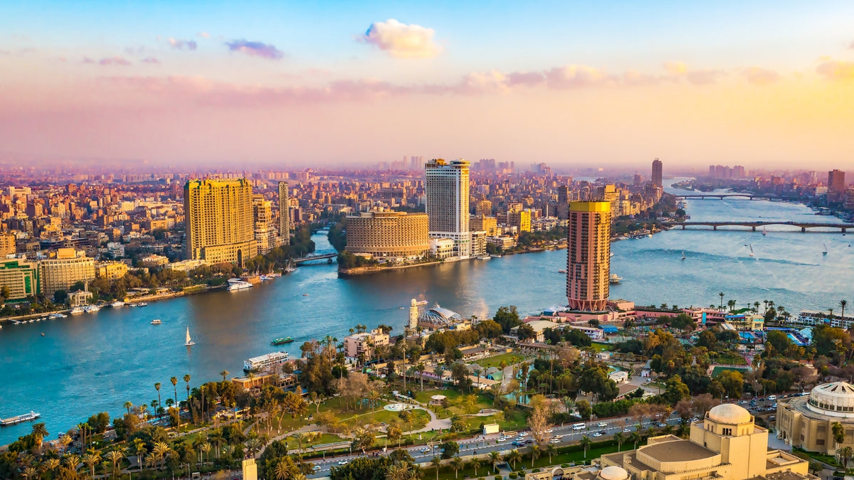 Panoramic aerial view of the Nile River flowing through Cairo, Egypt, featuring the city skyline, bridges, luxury hotels, and vibrant sunset over one of the world's longest rivers.