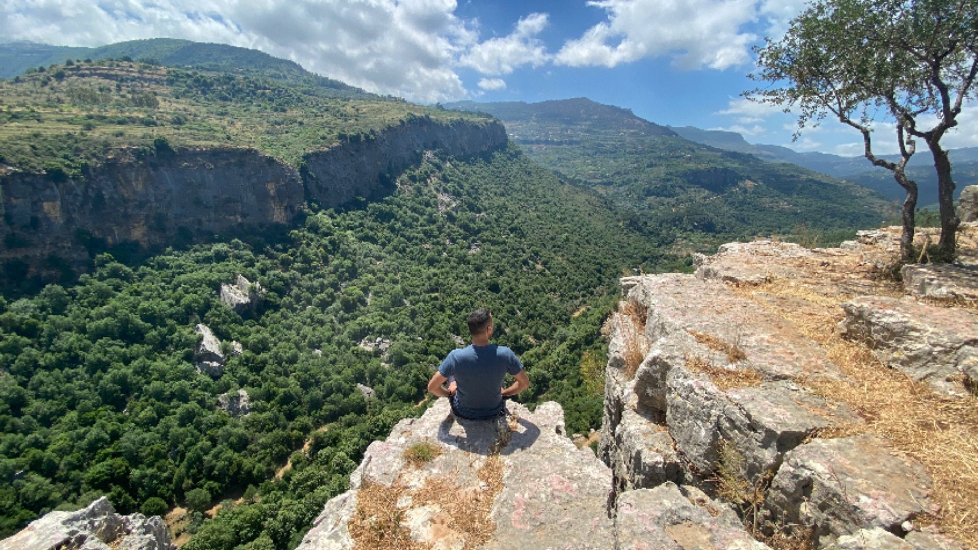Person sitting on a rocky outcrop overlooking bisri valley with green mountains in al chouf lebanon