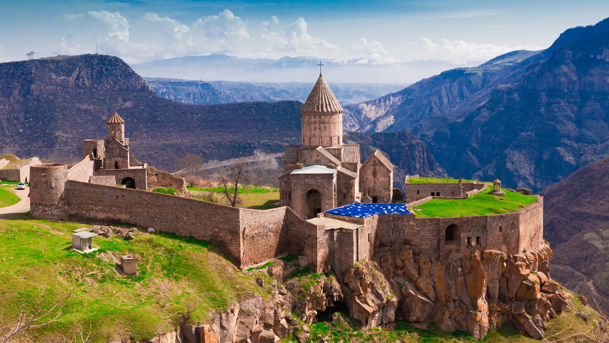 Panoramic view of Tatev Monastery perched on a cliff in Syunik Province, Armenia, surrounded by dramatic mountain landscapes and deep canyons under a blue sky.