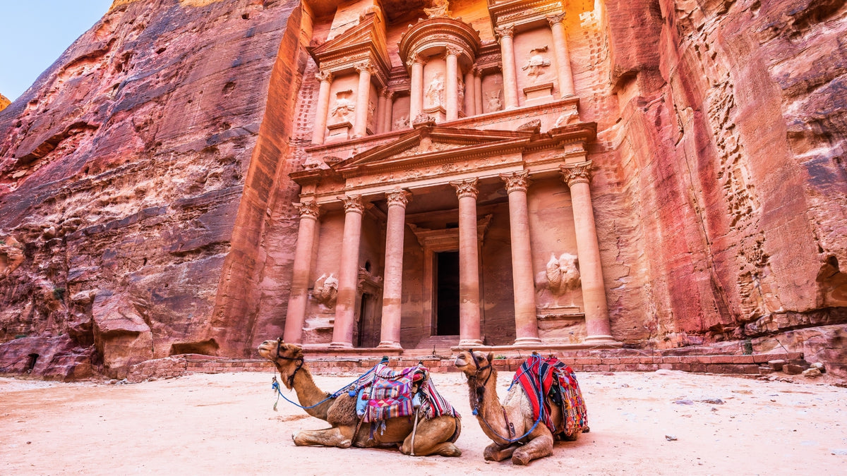 The Treasury (Al-Khazneh) in Petra, Jordan, with two camels resting in front of the iconic ancient rock-carved façade, one of the New Seven Wonders of the World.