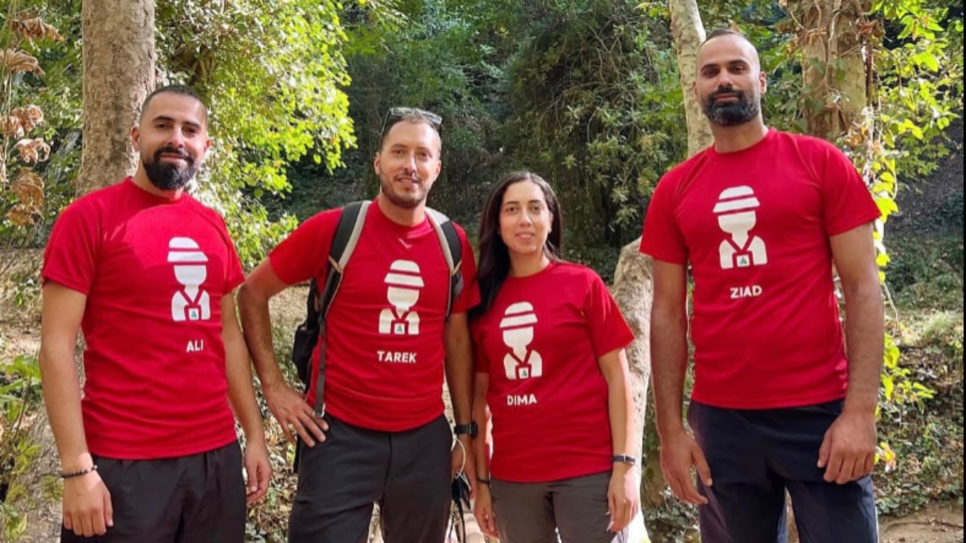 Four people wearing red t-shirts with a logo and text in a forest setting representing True Adventure Lebanon